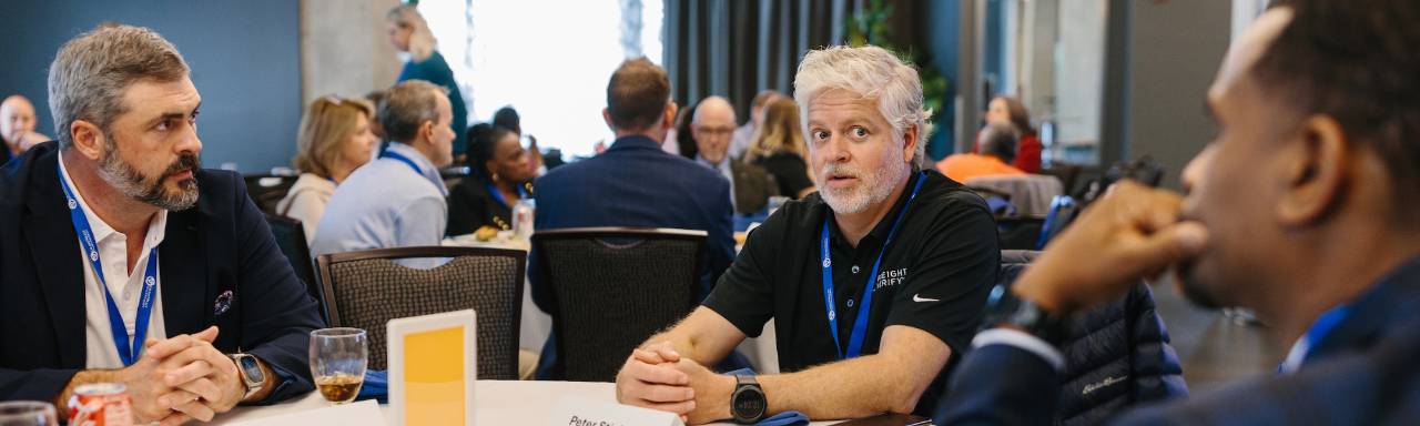 Three men seated at a table talking about leadership best practices.